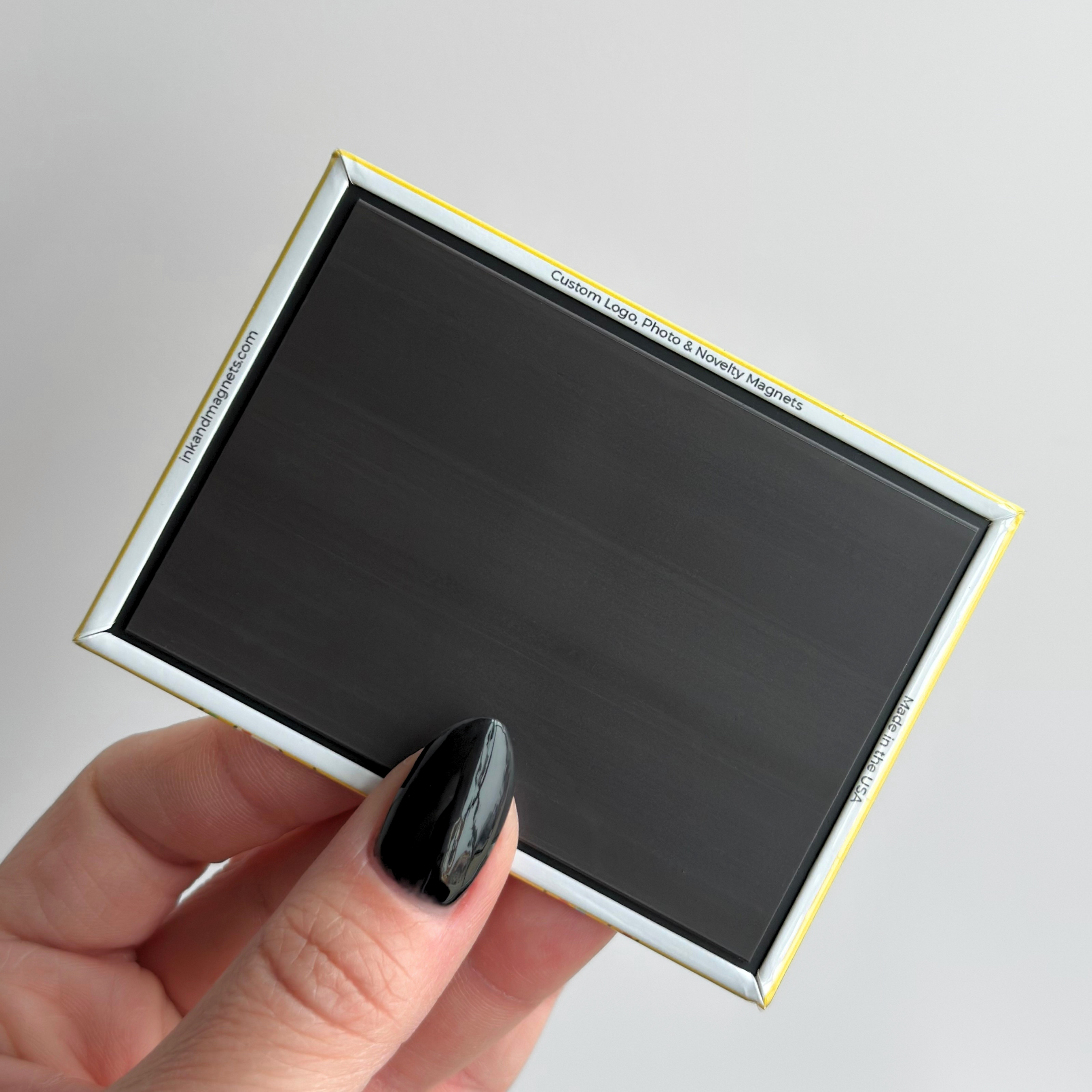 Hand holding a rectangular, retail-style button magnet showcasing the back which features a closed corner professional finish and strong rubber magnet.