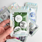 Cannabis culture novelty magnet pack held in hand, featuring humorous weed-themed fridge magnets in collectible magnet sets also available as a pin pack.