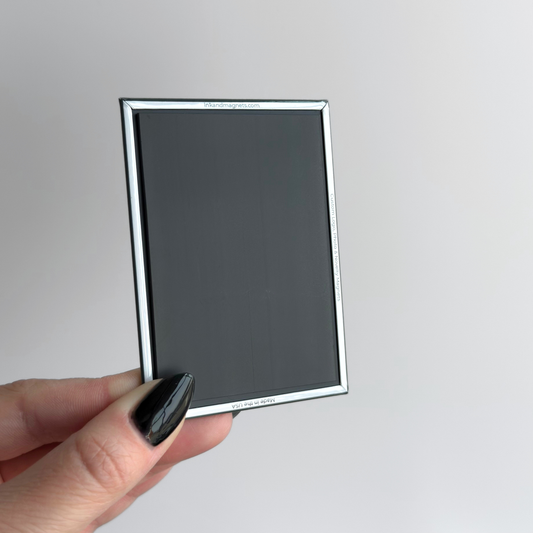 Hand holding a button magnet featuring the backside that includes a closed corner design and a full size, strong rubber magnet. Shown in a rectangular format.