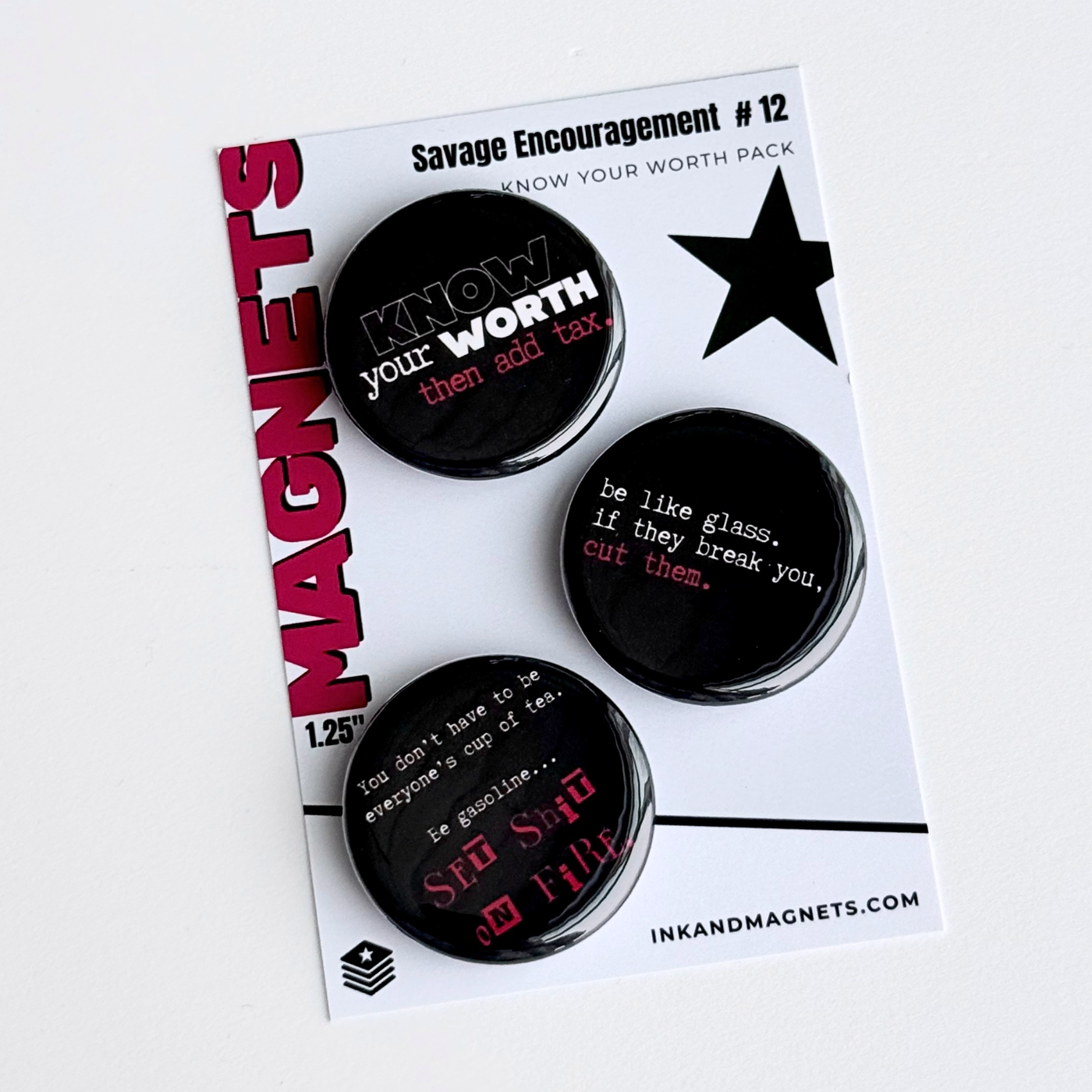 Set of three black button style fridge magnets with motivational phrases on an ink and magnets branded retail card.