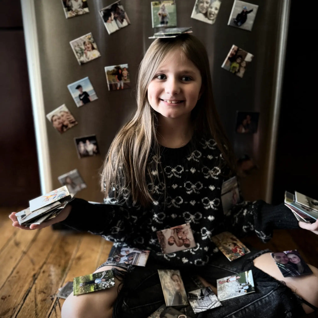 Child holding piles of photo magnets with a fridge magnet display behind her. Cozy decor when one photo magnet isn't enough.