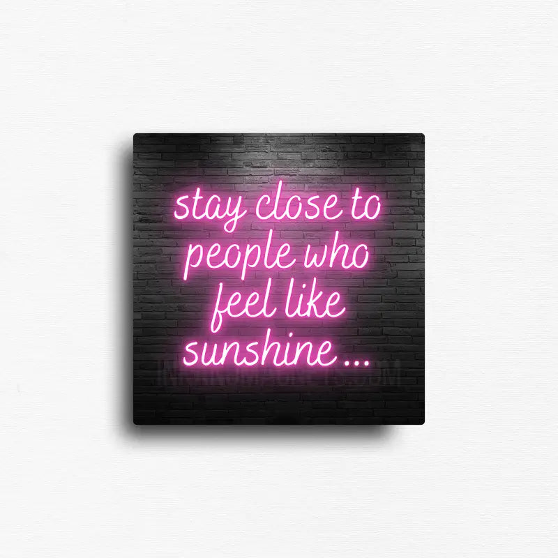 Modern neon friendship quote button magnet featuring glowing pink script that reads "Stay close to people who feel like sunshine" on a dark brick wall background. Decorative encouragement magnet for refrigerators, lockers, office file cabinets, magnetic boards, dorm rooms, and workspaces.