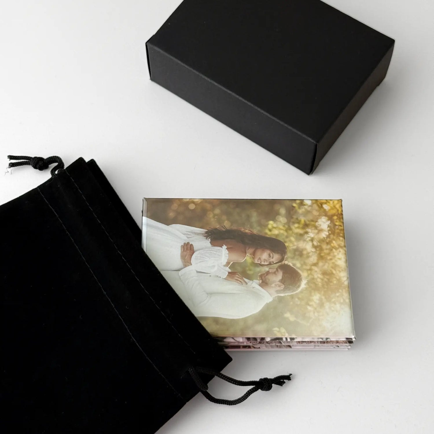 Custom photo magnets displayed with a black gift box and drawstring pouch. Personalized photo keepsakes ready for gifting to family and friends for birthdays, holidays, anniversaries, and other special occasions.