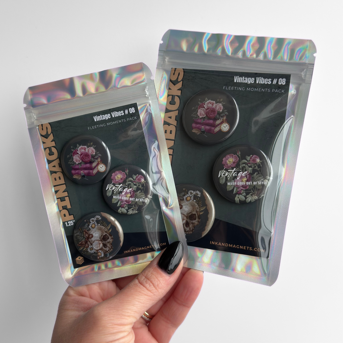 Hand holding vintage vibes pinback button badges in retail packaging featuring green pins with floral designs.