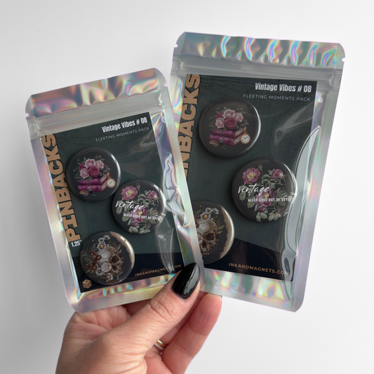 Hand holding vintage vibes pinback button badges in retail packaging featuring green pins with floral designs.