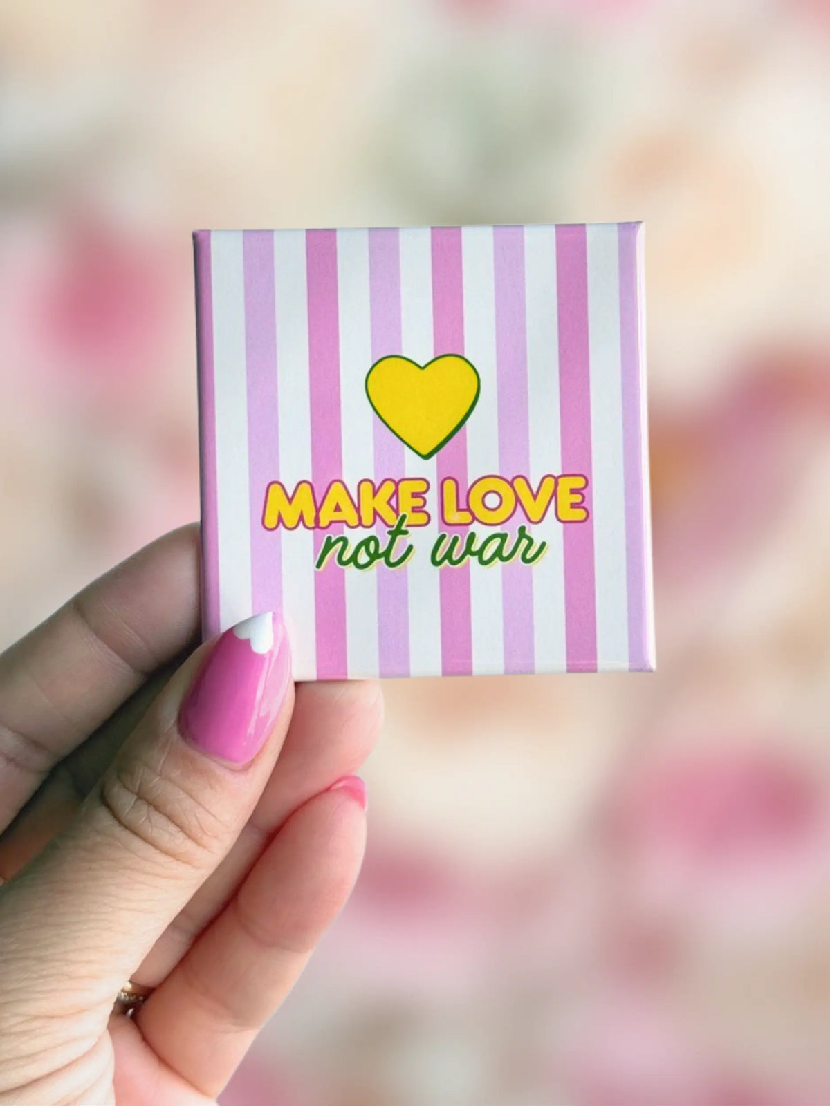 Hand holding a colorful kindness quote fridge magnet from the Love Notes + Pep Talks novelty magnet collection featuring the message "Make Love, Not War."