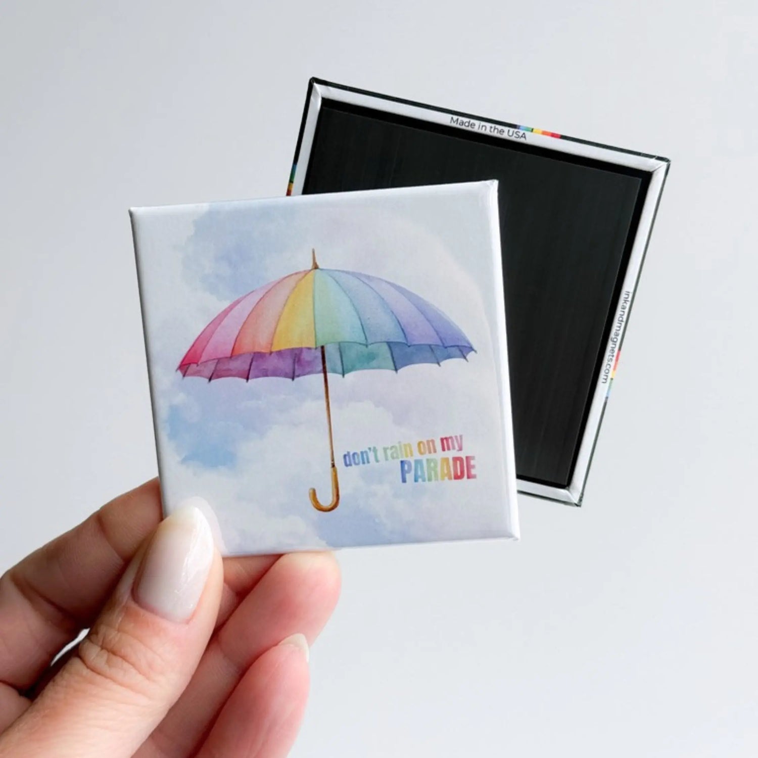Square Pride button fridge magnet with a watercolor rainbow umbrella and “Don’t Rain on My Parade” design, shown with the rigid hard back and full magnet backing. A ready-made novelty magnet for fridges, lockers, magnetic boards, or small gifts.