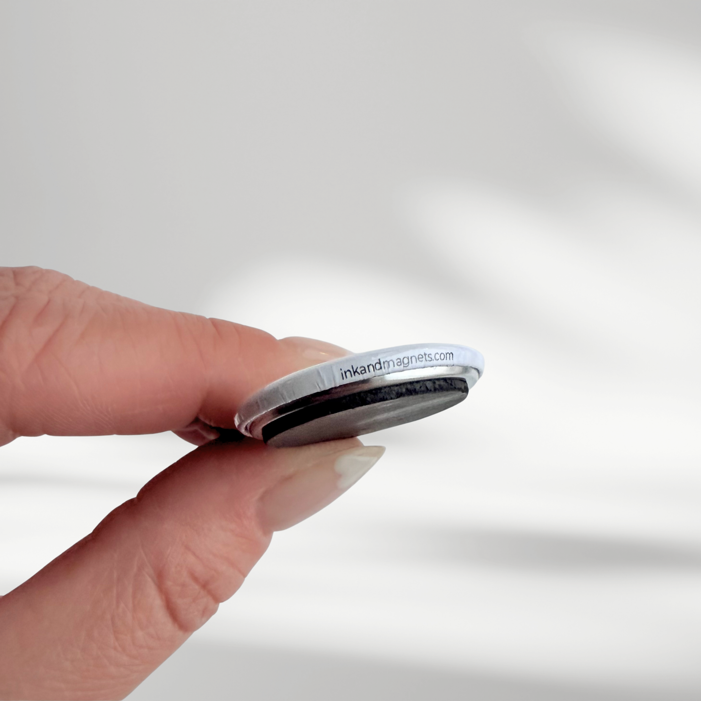 Hand holding a small button magnet showcasing a thick durable magnet used to make the ink and magnets 1.25" button packs.